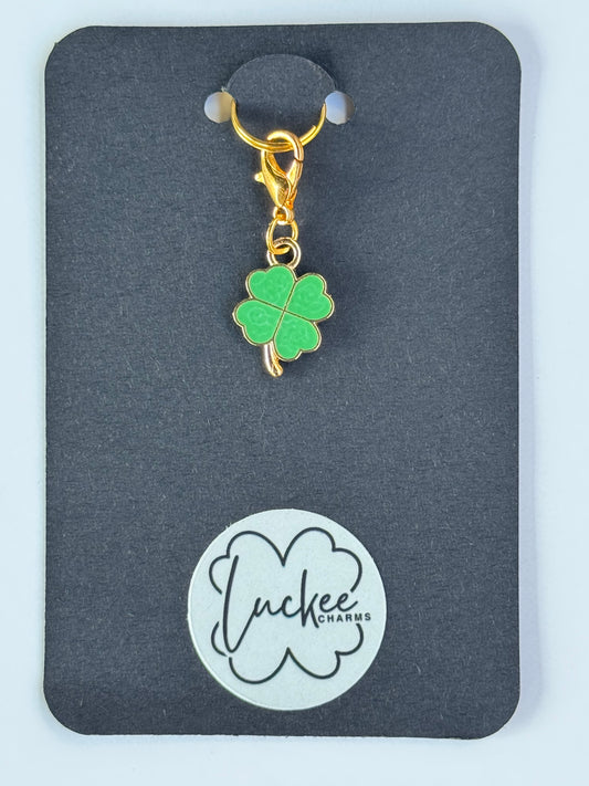 Green four-leaf clover charm on a black card with a brand logo.