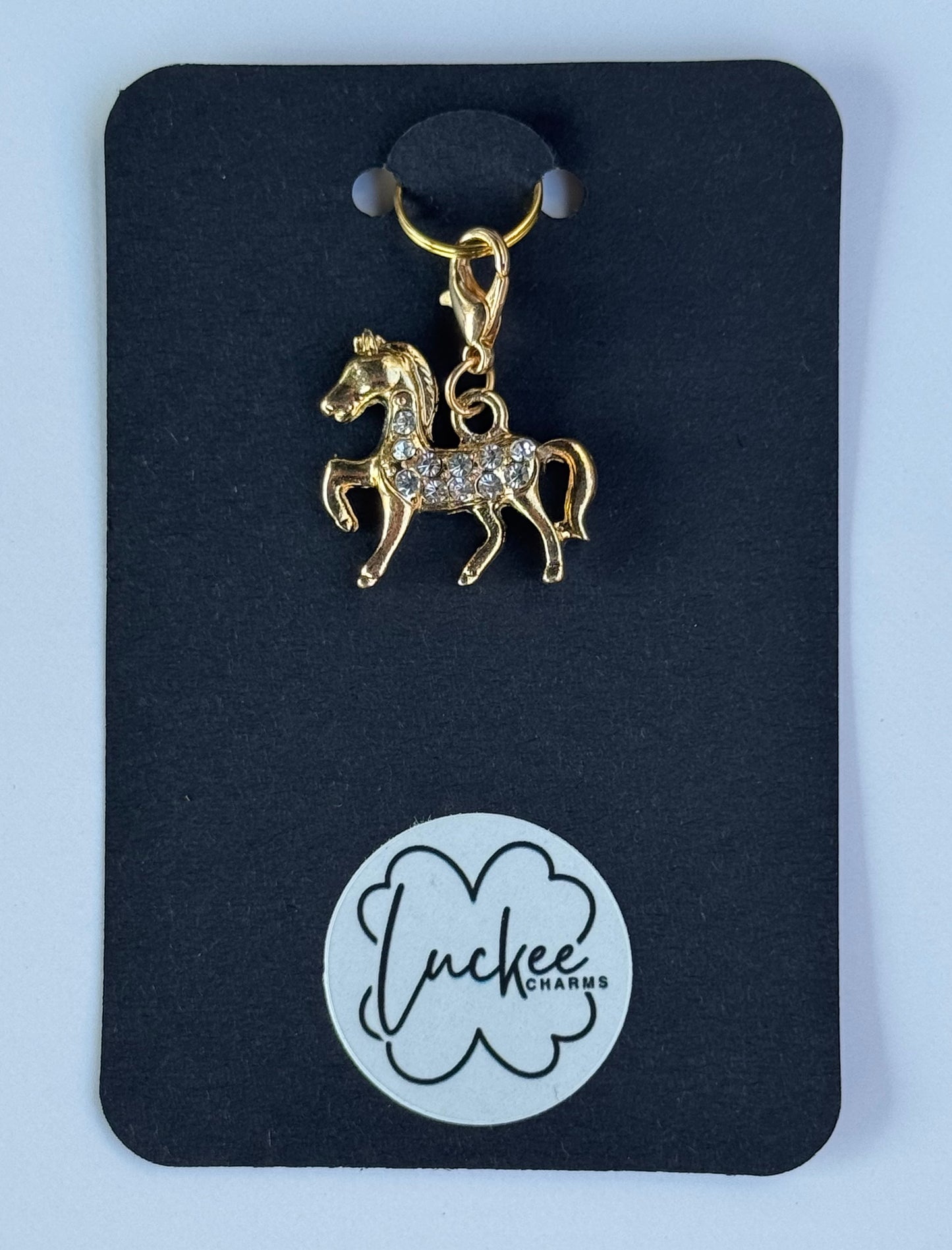 Gold horse-shaped charm on a black card with 'Luckee Charms' branding.