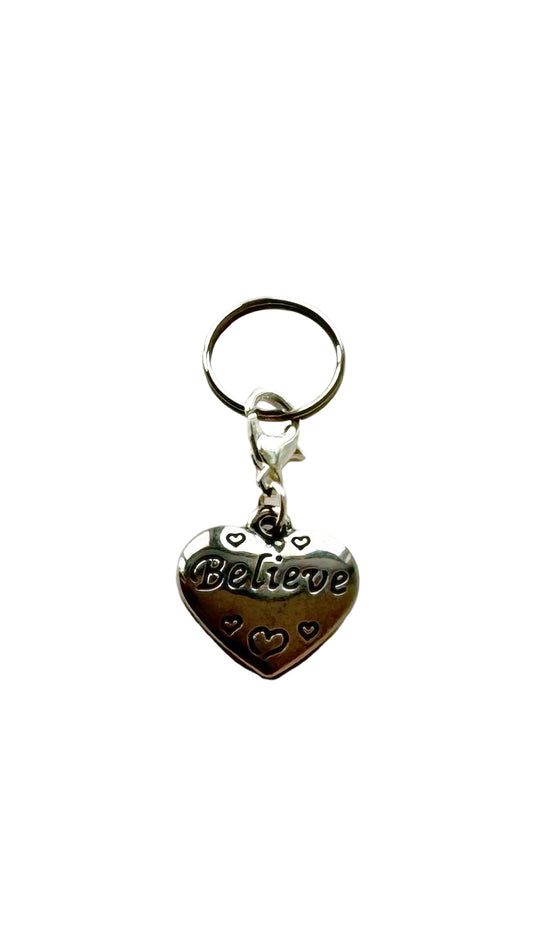 Silver heart-shaped charm with 'Believe' engraving on a white background