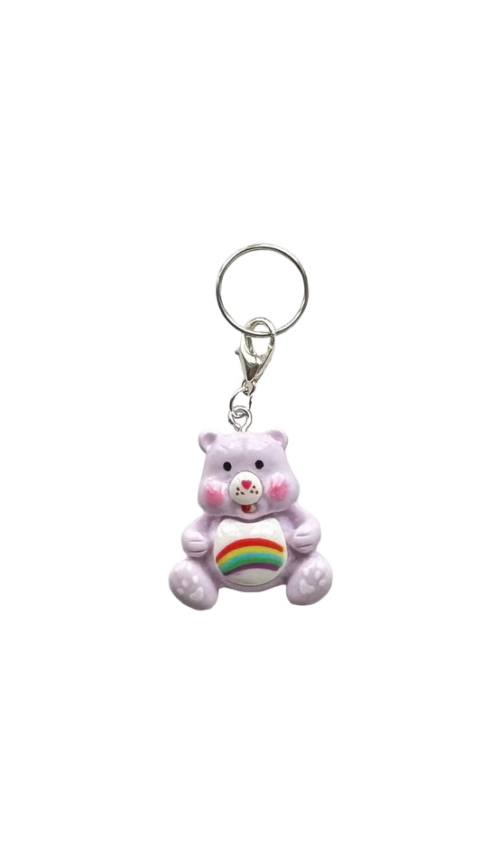 Purple teddy bear charm with a rainbow heart on a white background
