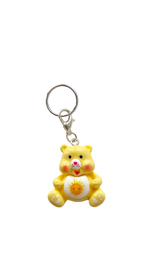 Yellow teddy bear charm with a sun on a white background