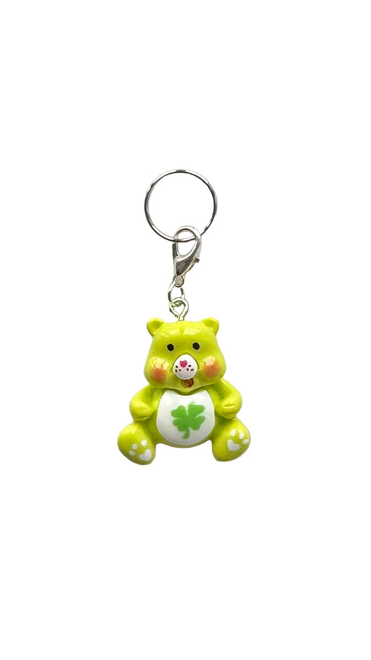 Green teddy bear charm with a four-leaf clover on a white background