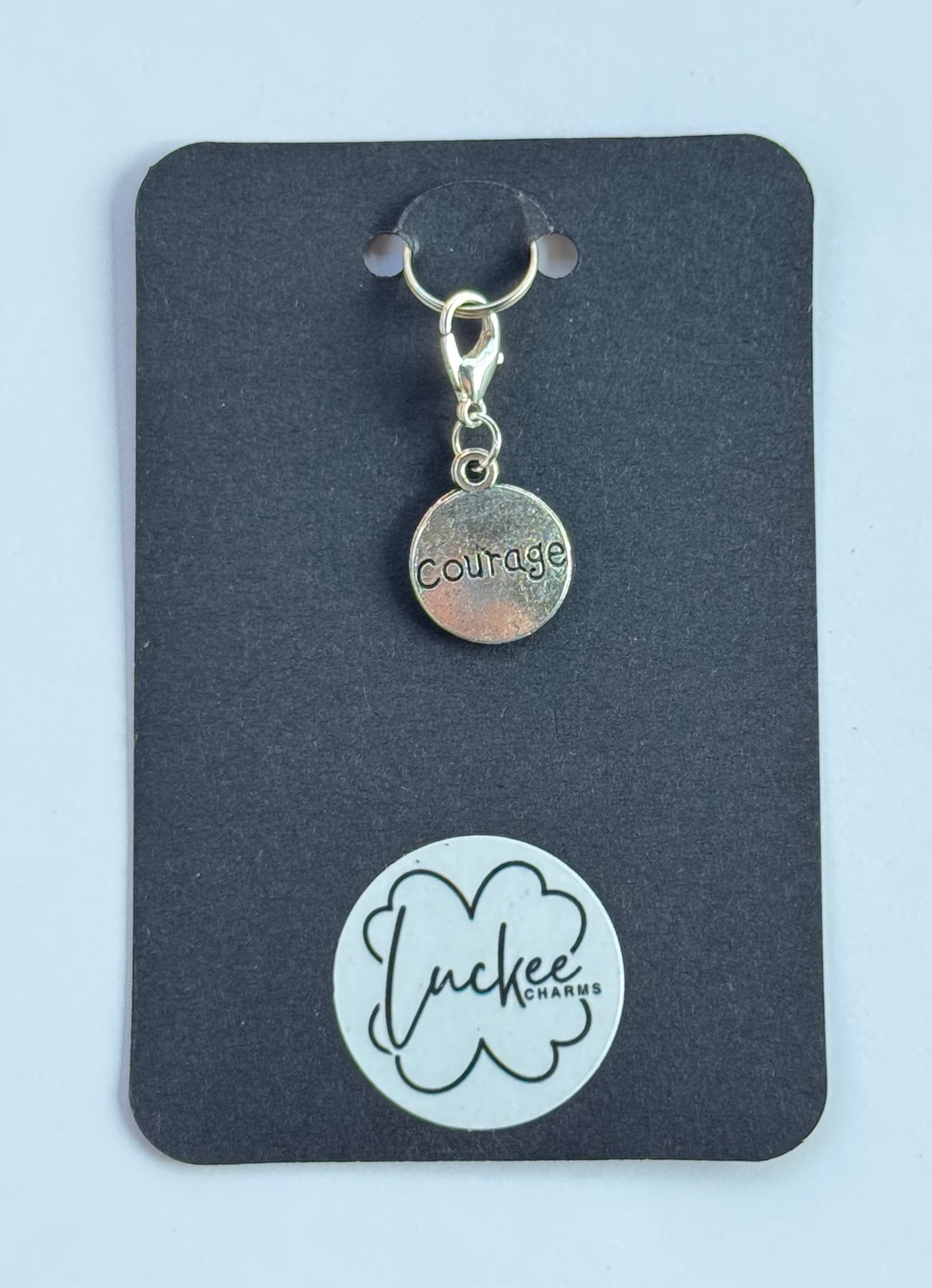Silver 'courage' charm on a black card with Luckee Charms logo
