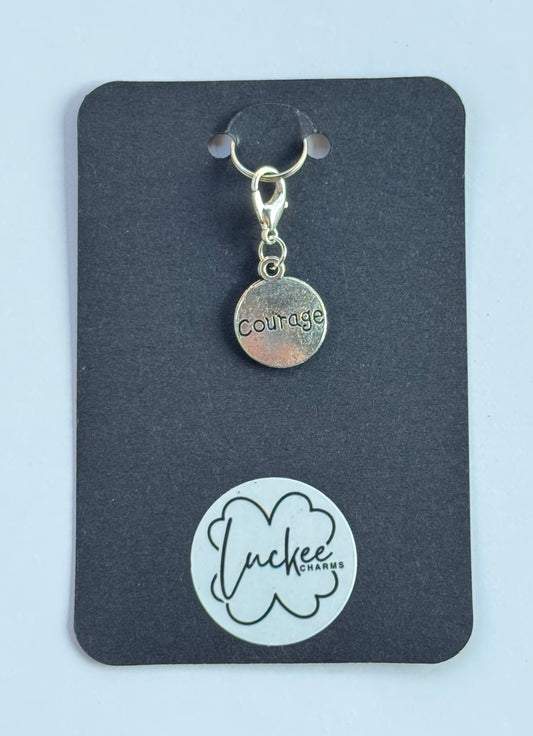 Silver 'courage' charm on a black card with Luckee Charms logo