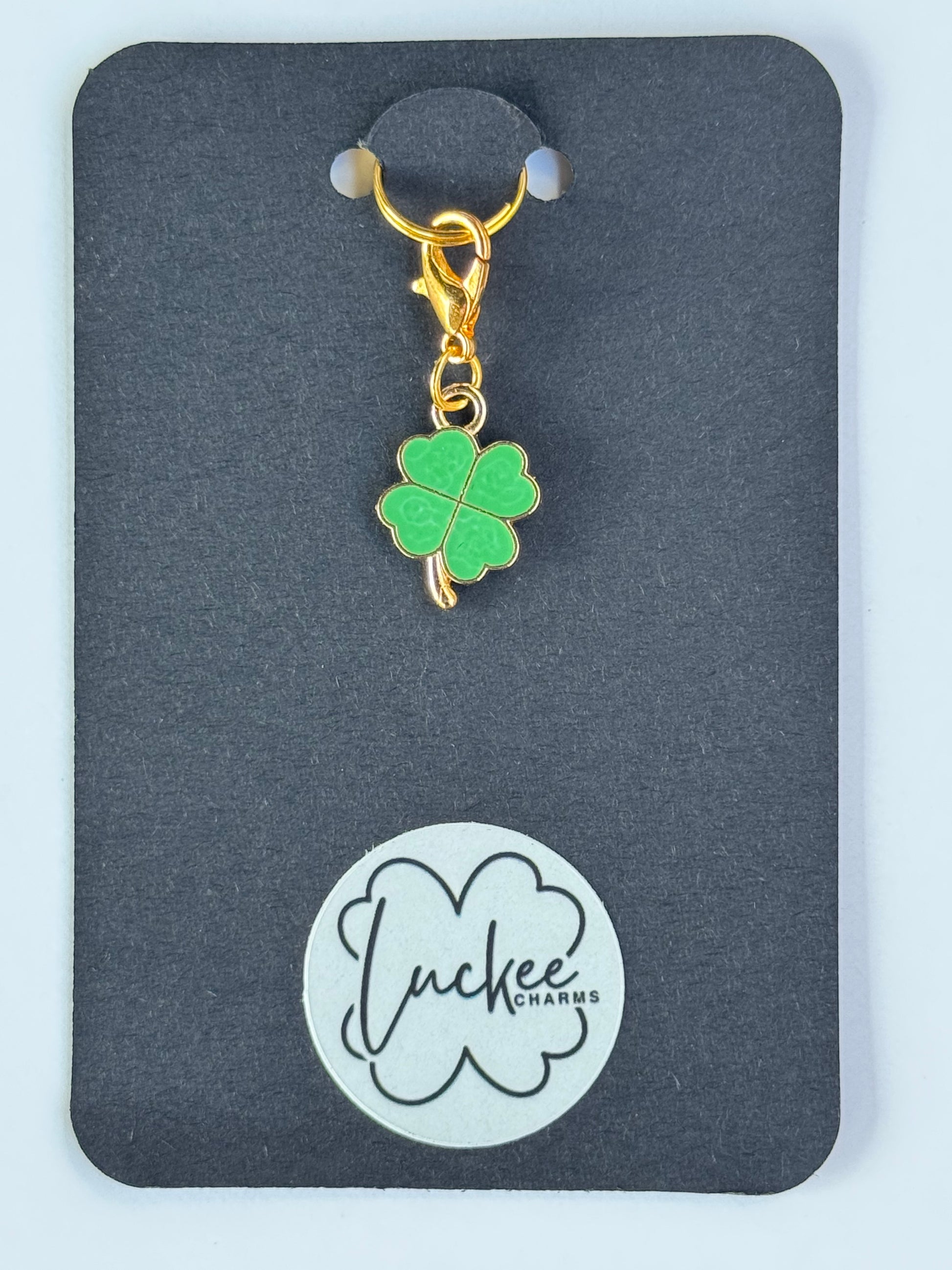 Green four-leaf clover charm on a black card with a brand logo.