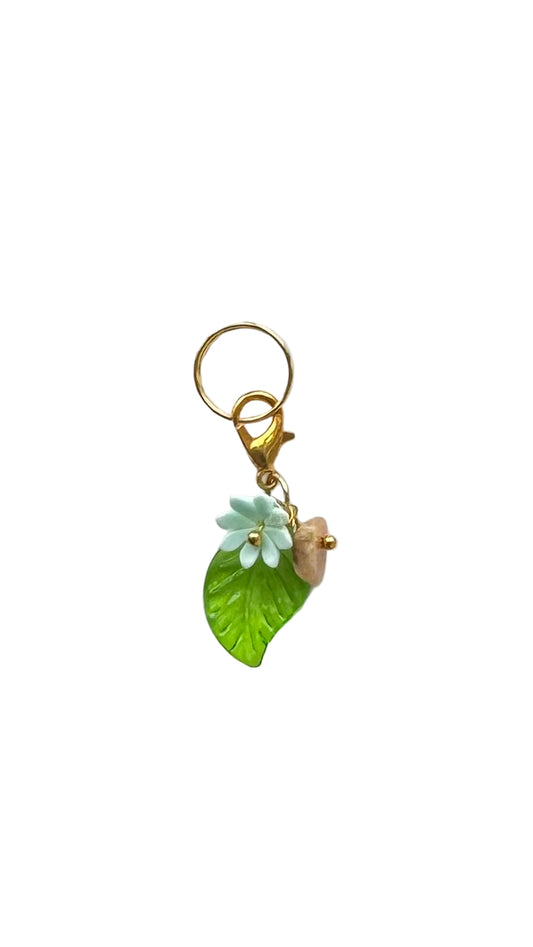 Decorative keychain with green leaf and white flower charm on a light gray background