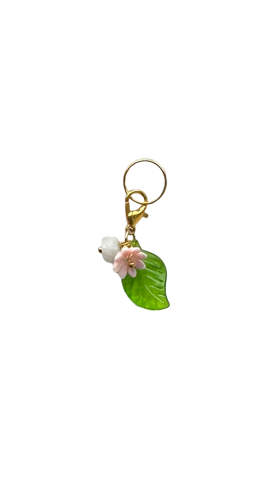 Small decorative charm with a flower and green leaf on a light gray background