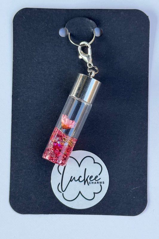 Charm in the shape of a small bottle with a pink flower on a black card with a brand logo.