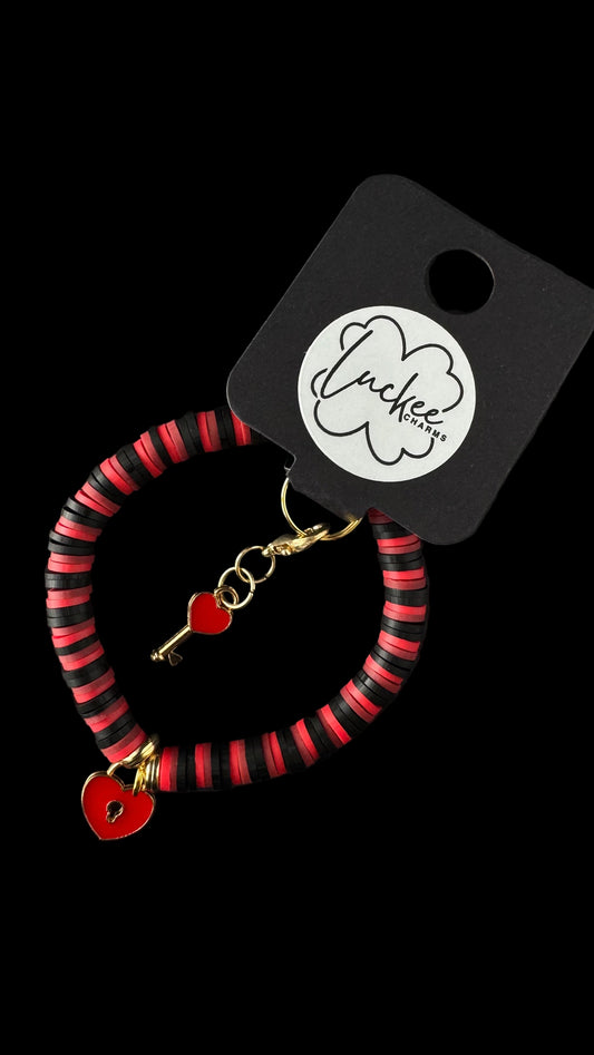 Black and red striped bracelet with heart and key charms on a black background.