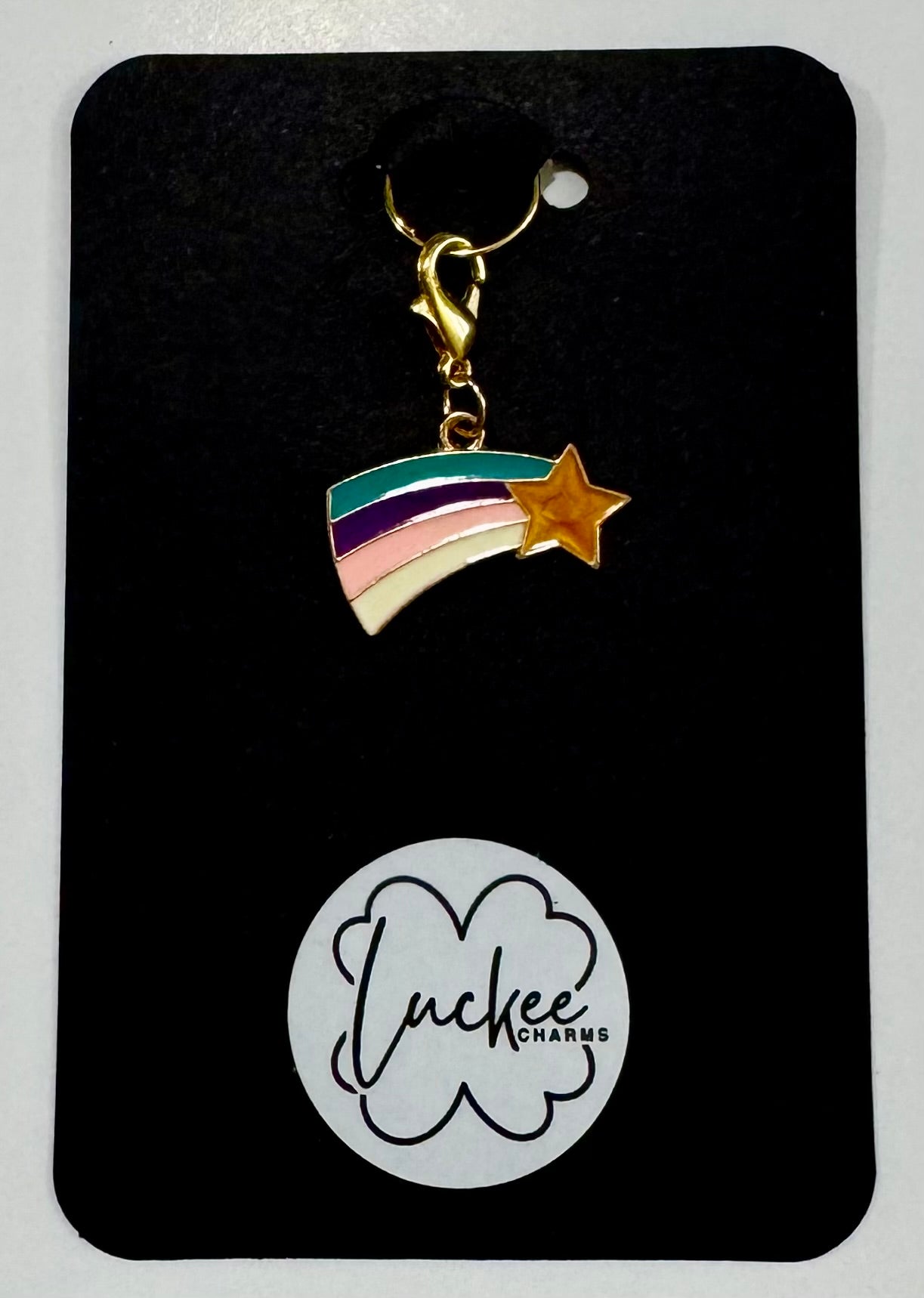 Rainbow charm with star on a black card featuring 'Luckee Charms' logo