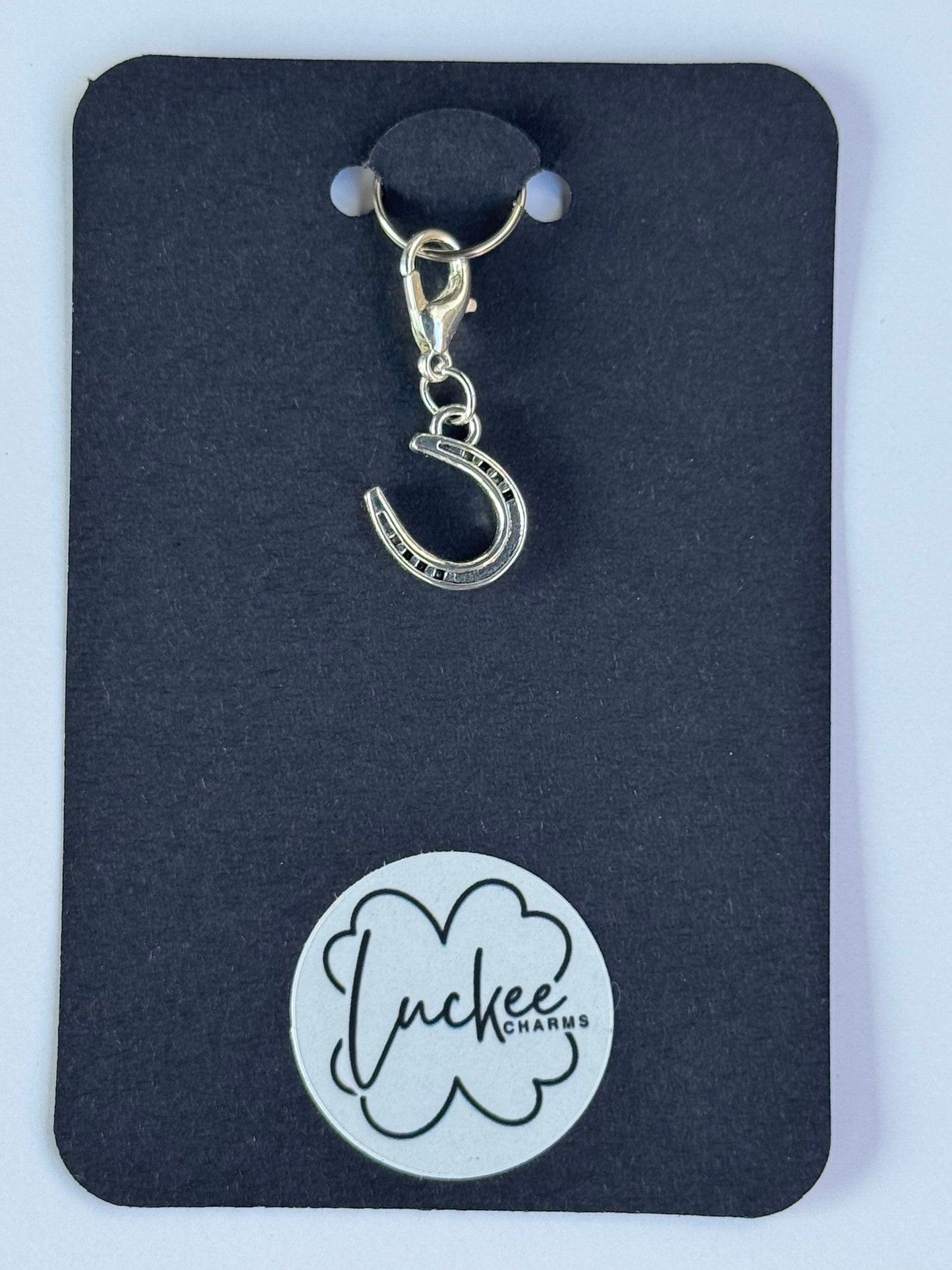 Silver charm with a horseshoe design on a black card with a brand logo.