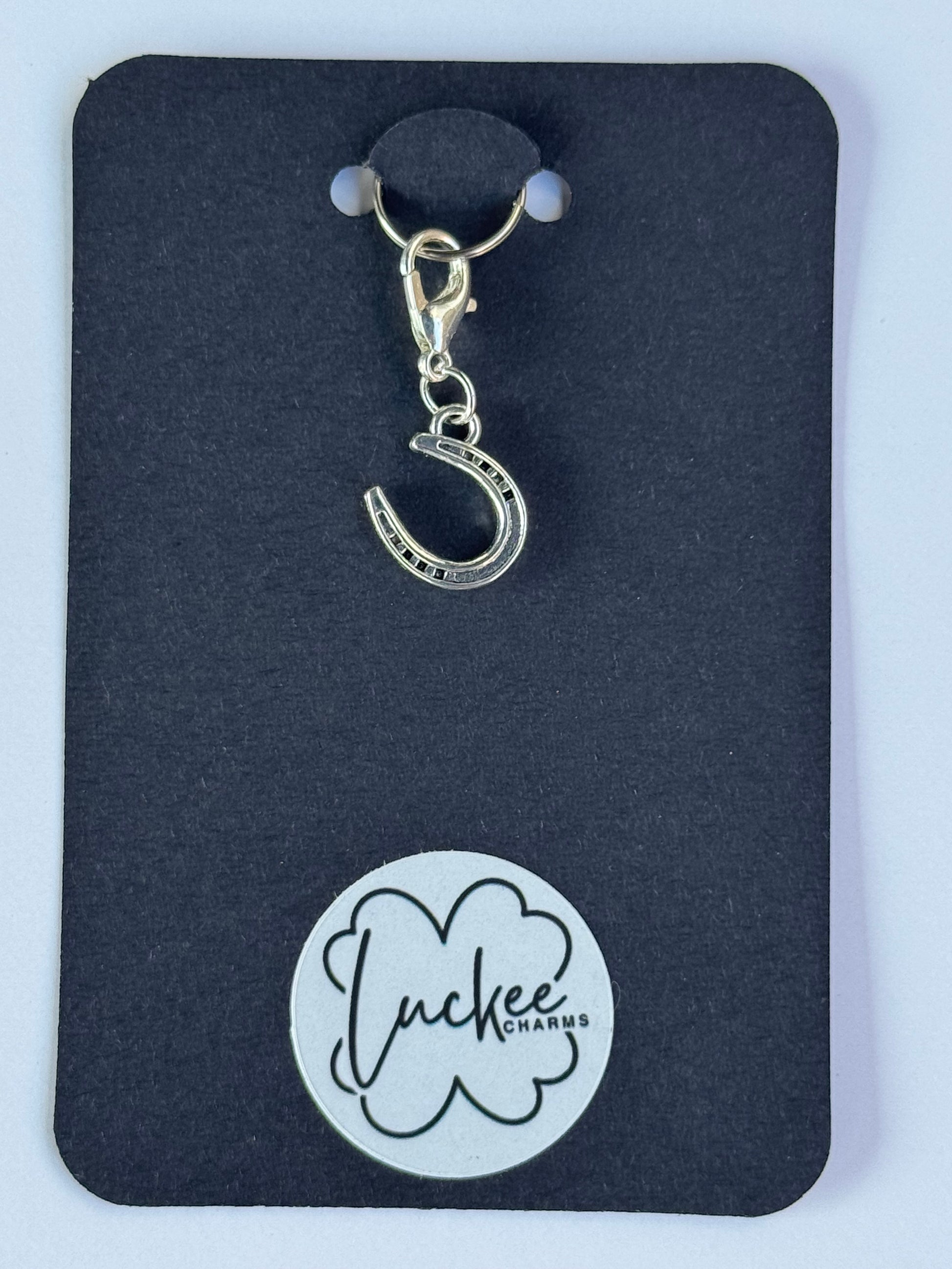 Silver charm with a horseshoe design on a black card with a brand logo.