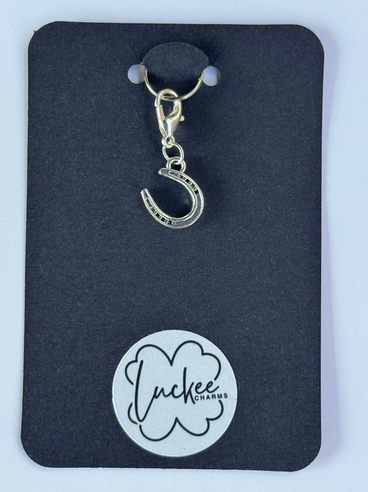 Silver charm with a horseshoe design on a black card with a brand logo.