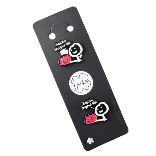 Two pins with cartoon designs on a black card with a brand logo.